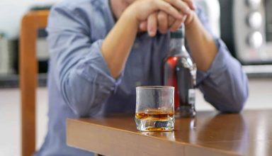 A man with bottle of whiskey on the kitchen. The concept of drunkenness and alcoholism. Alcoholic father.