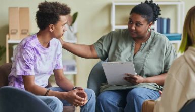 African young psychologist talking to teenage boy during therapy session at classroom